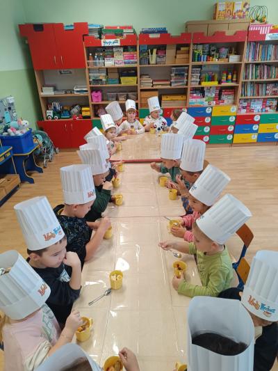 Przedszkolaki jedzą sałatkę owocową  kubeczków.