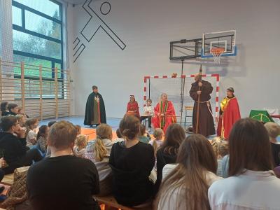 Uczniowie siedzą. Na scenie stoją m.in.: biskup, zakonnik, Dobrawa, Mieszko I, Bolesław Chrobry.