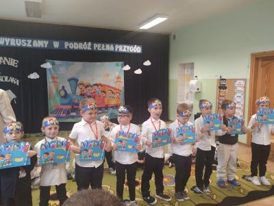 Przedszkolaki stoją na scenie i trzymają w dłoniach upominki.