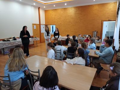 Uczniowie siedzą przy stołach i słuchają pani psycholog.