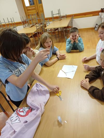 Uczniowie sklejają taśmą podartą kartkę papieru.