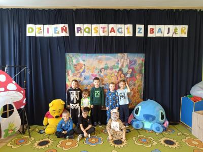 Przedszkolaki przebrane za postacie z bajek stoją na tle postaci z bajek Disney'a.