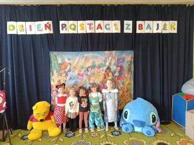 Przedszkolaki przebrane za postacie z bajek stoją na tle postaci z bajek Disney'a.