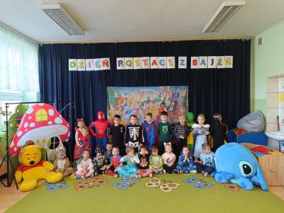 Przedszkolaki przebrane za postacie z bajek stoją na tle postaci z bajek Disney'a.