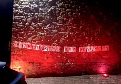 Budynek szkoły podświetlony na czerwono. Na budynku umieszczono napis: Dzieciństwo bez przemocy.