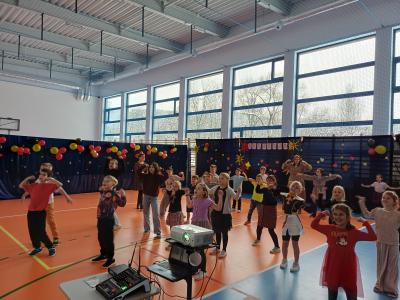 Uczniowie tańczą razem z wyświetlanymi na ekranie instruktorami tańca.