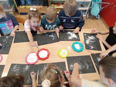 Przedszkolaki malują solą na czarnych kartkach.