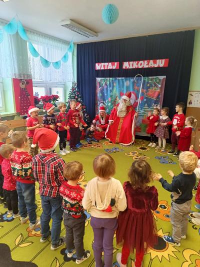 Mikołaj siedzi w kole, a dzieci stoją.