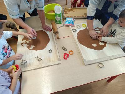 Dzieci wykrawają foremkami pierniczki w cieście.