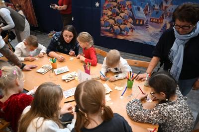 Rodzice wraz z dziećmi kolorują drewniane ozdoby.