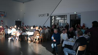 Dziadkowie siedzą za stołami, oglądają przedstawienie i częstują się poczęstunkiem.