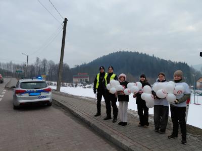 Uczniowie wraz z policjantami stoją przed przystankiem autobusowym.
