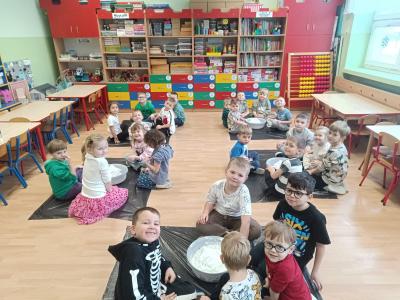 Przedszkolaki siedzą w grupkach na podłodze, a w miskach znajduje się piankolina.