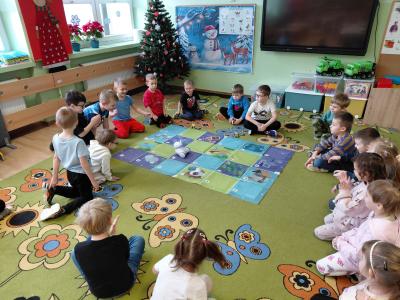 Dzieci siedzą w kole na dywanie, pośrodku nich znajduje się robot Photon i mata edukacyjna.