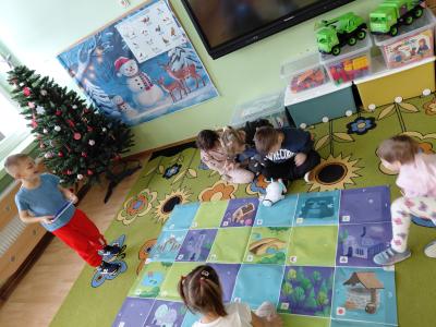 Dzieci siedzą w kole na dywanie, a jedno dziecko programuje trasę robota Photon po macie edukacyjnej.