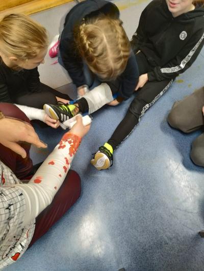 Uczniowie pod okiem pielęgniarki bandażują nogę.