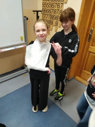 Uczennica uczy się zakładania temblaka na swojej koleżance.