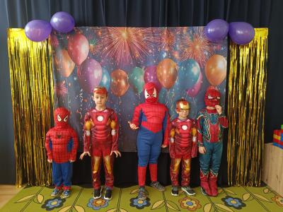 Dzieci przebrane za postacie z gier i bajek stoją na karnawałowym tle z balonami.