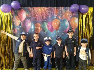 Dzieci przebrane za policjantów stoją na karnawałowym tle z balonami.