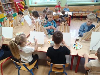 Dzieci malują farbami na płótnie, na sztalugach.