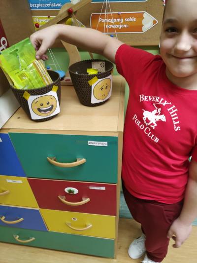 Dziecko wkłada opakowanie po przekąsce do uśmiechniętego koszyka.