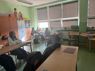 Uczniowie siedzą w ławkach i słuchają prezentacji.