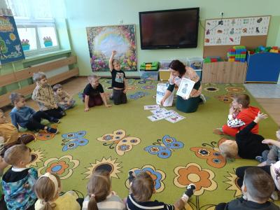 Dzieci siedzą w kole, a pani trzyma w dłoni kardy pokazowe.