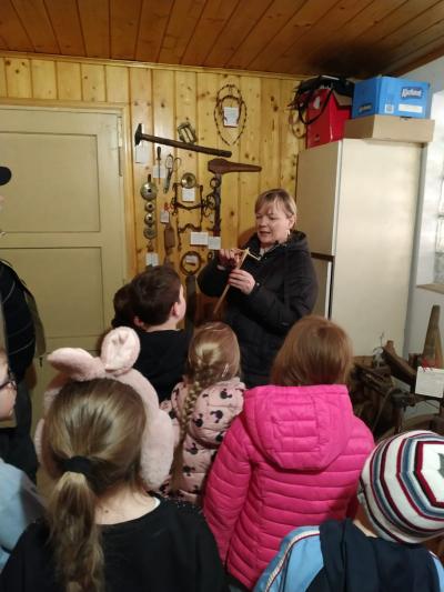 Uczniowie słuchają, jak pani Kasia prezentuje przedmioty dawnego użytku.