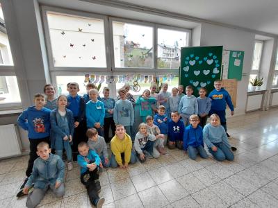 Uczniowie ubrani na niebiesko stoją na tle wykonanych przez siebie papierowych skarpet oraz tablicy z niebieskim serduszkiem.