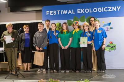 Jury i uczniowie z dyplomami i nagrodami stoją na scenie.