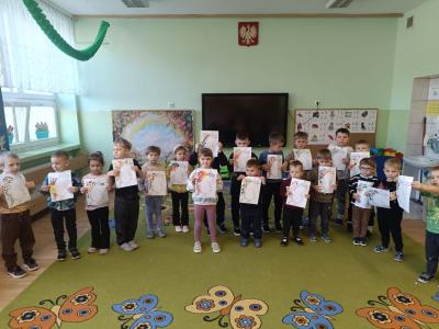 Dzieci stoją w grupie i trzymają prace- wyklejone kropkami grzywy Gucia.