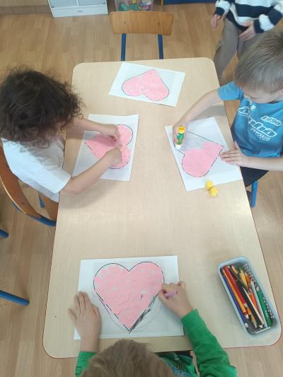 Dzieci wyklejają duże serce małymi serduszkami z dziurkacza.