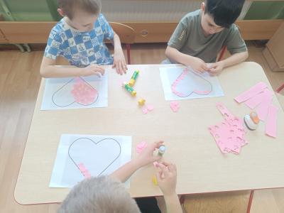 Dzieci wyklejają duże serce małymi serduszkami z dziurkacza.