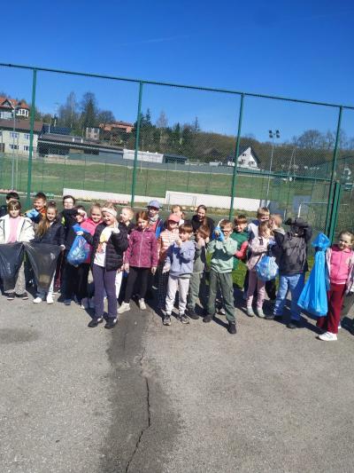 Uczniowie stoją w grupie ze zebranymi w workach śmieciami.