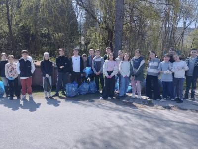 Uczniowie stoją w grupie z zebranymi w workach śmieciami.