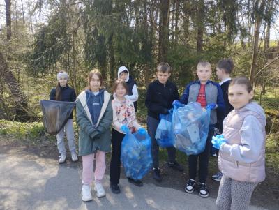 Uczniowie stoją w grupie z zebranymi w workach śmieciami.