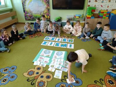 Dziecko wykonuje zadanie na dywanie, a reszta dzieci siedzi w kole na dywanie.