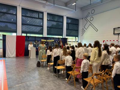 Dyrekcja i zebrani stoją na baczność i śpiewają Hymn