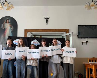 Uczniowie trzymają w dłoniach kartki ze słowami: pokój, pomoc, przebaczenie, odwaga, szacunek, miłość.