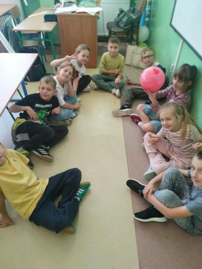 Uczniowie grają piłką siedząc na podłodze.